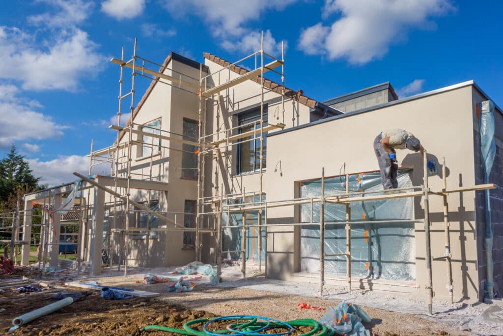 Ouvrier façadier appliquant l'enduit sur une maison moderne en construction avec échafaudage sous un ciel bleu nuageux. Chantier.